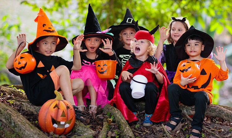 A group of young children dressed as devils and witches with orange jack-o-lantern candy buckets.