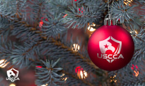 Image of Christmas tree branches with a red USCCA ornament in the front.