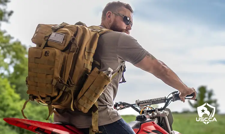 Build a bug-out or get-home bag for emergency preparedness — A man sits on a red motorcycle wearing a tactical backpack packed with survival essentials.